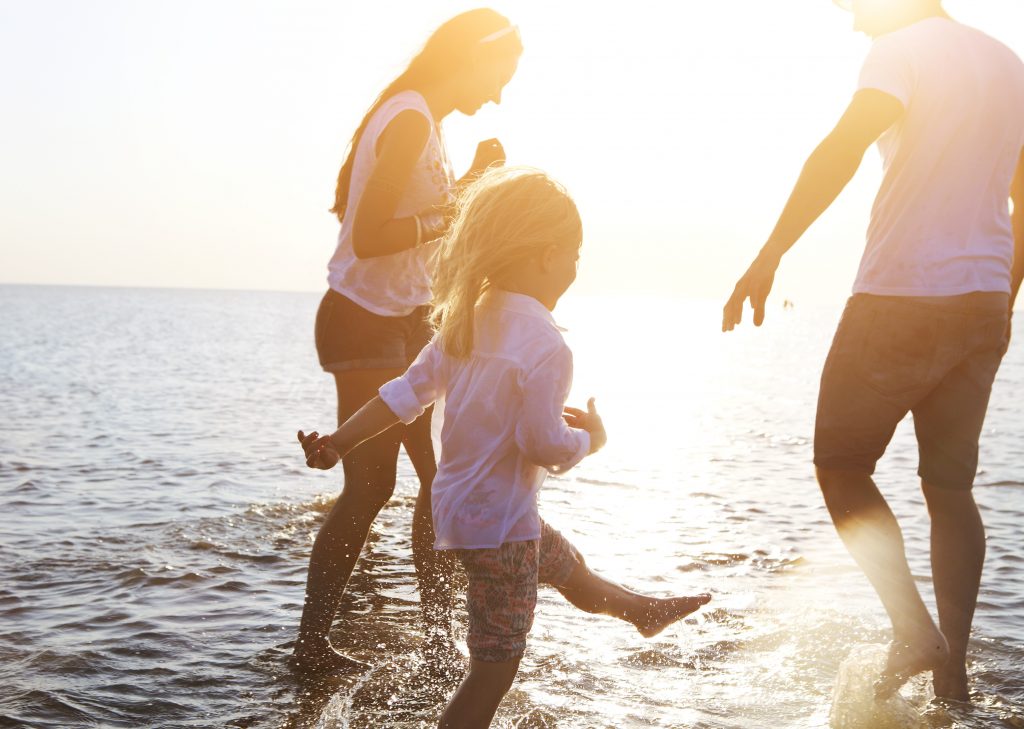 Happy young family having fun running on beach at sunset